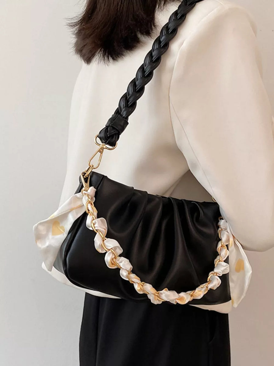 Black ruched shoulder bag with braided strap and decorative chain detail.
