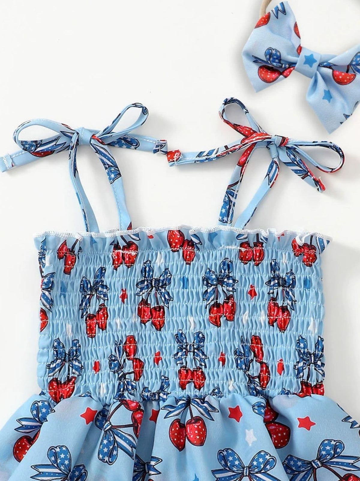 Baby bodysuit dress with cherry print, smocked bodice, and tie straps. Includes matching bow headband.