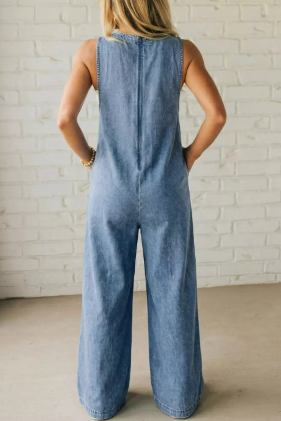 Denim jumpsuit with pintuck detail, tie v-neck, sleeveless, wide leg, and pockets.
