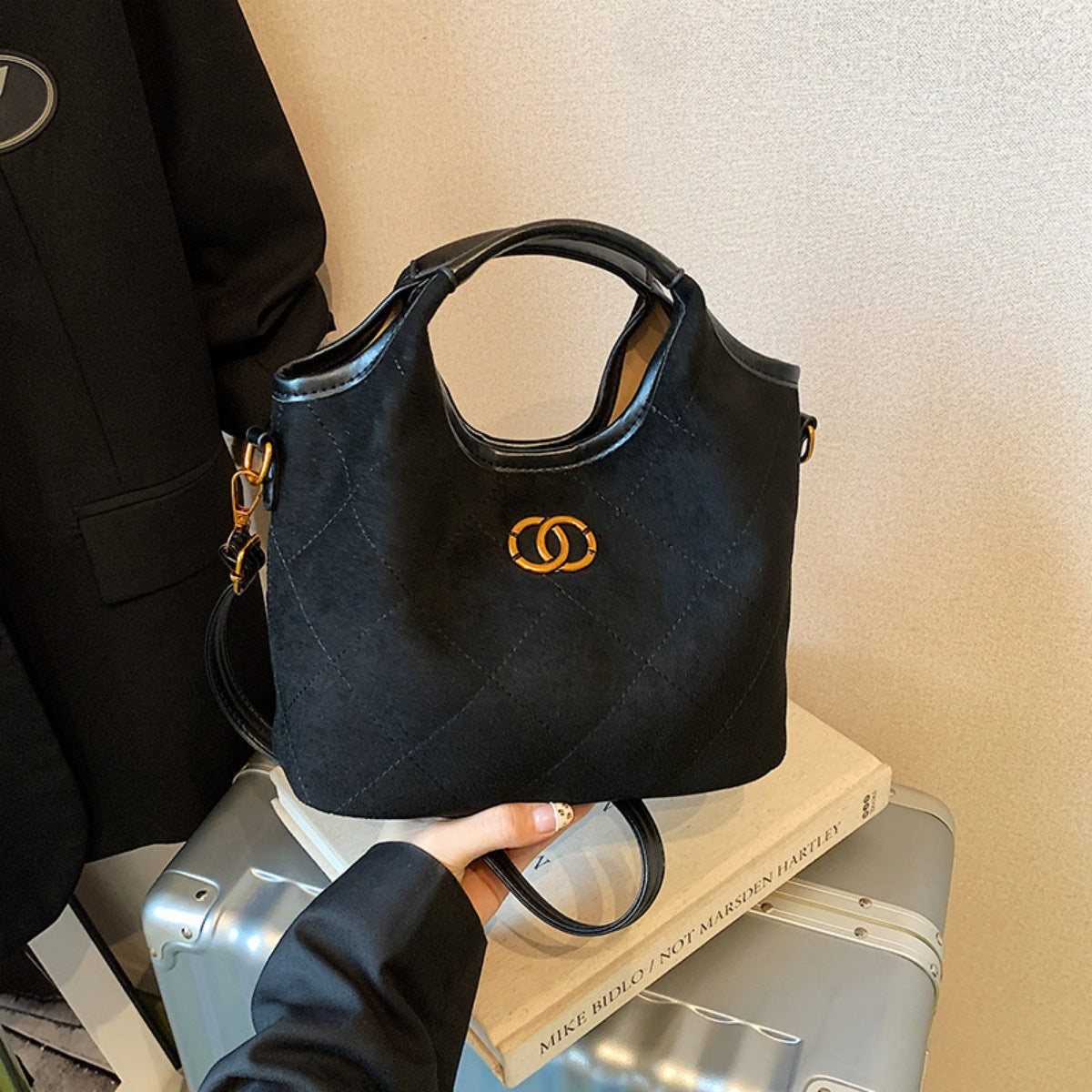 Black quilted suede tote bag with diamond pattern and gold logo detail.
