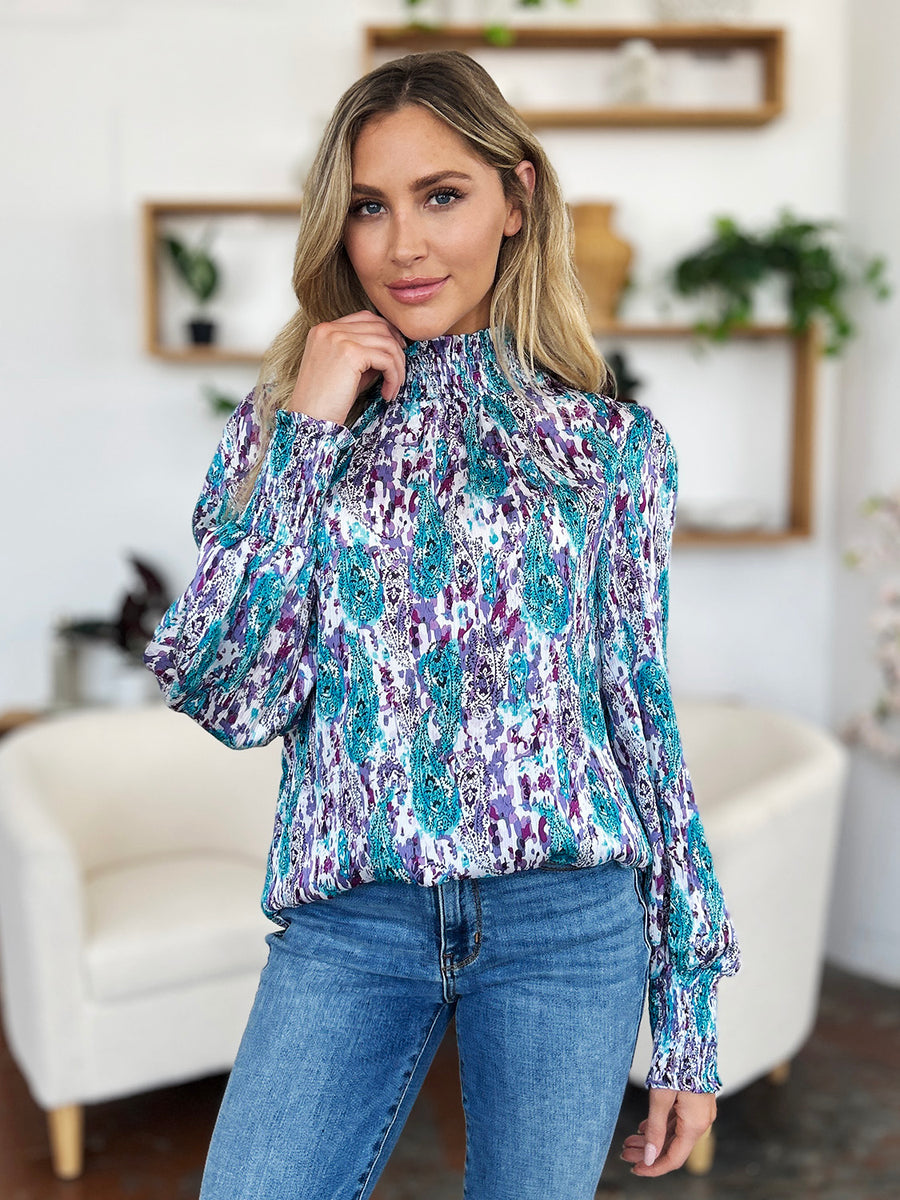 High neck abstract print blouse with smocked cuffs and neckline in blue, purple, and white.