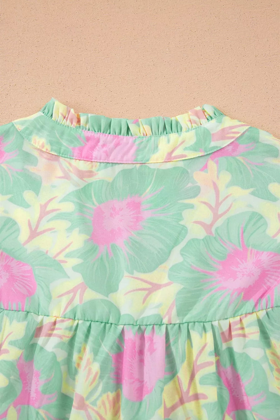 Pastel floral print polyester blouse with ruffled mock neck and tiered hem.