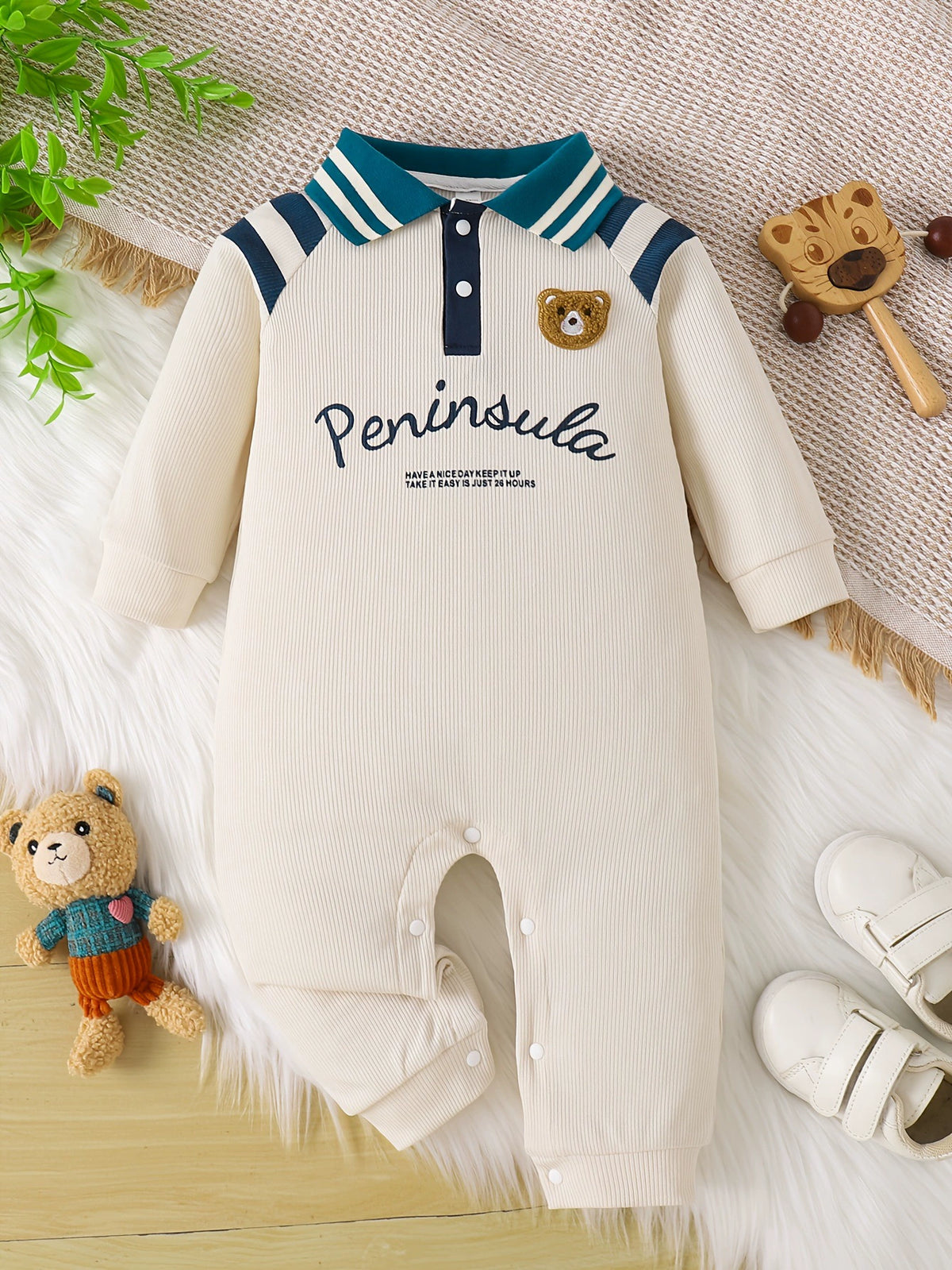 Baby long-sleeve one-piece in beige ribbed knit with striped collar and bear patch.