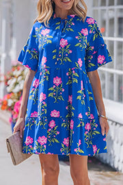 Tiered floral cotton dress with ruffle sleeves and tie neck in blue with pink flowers.