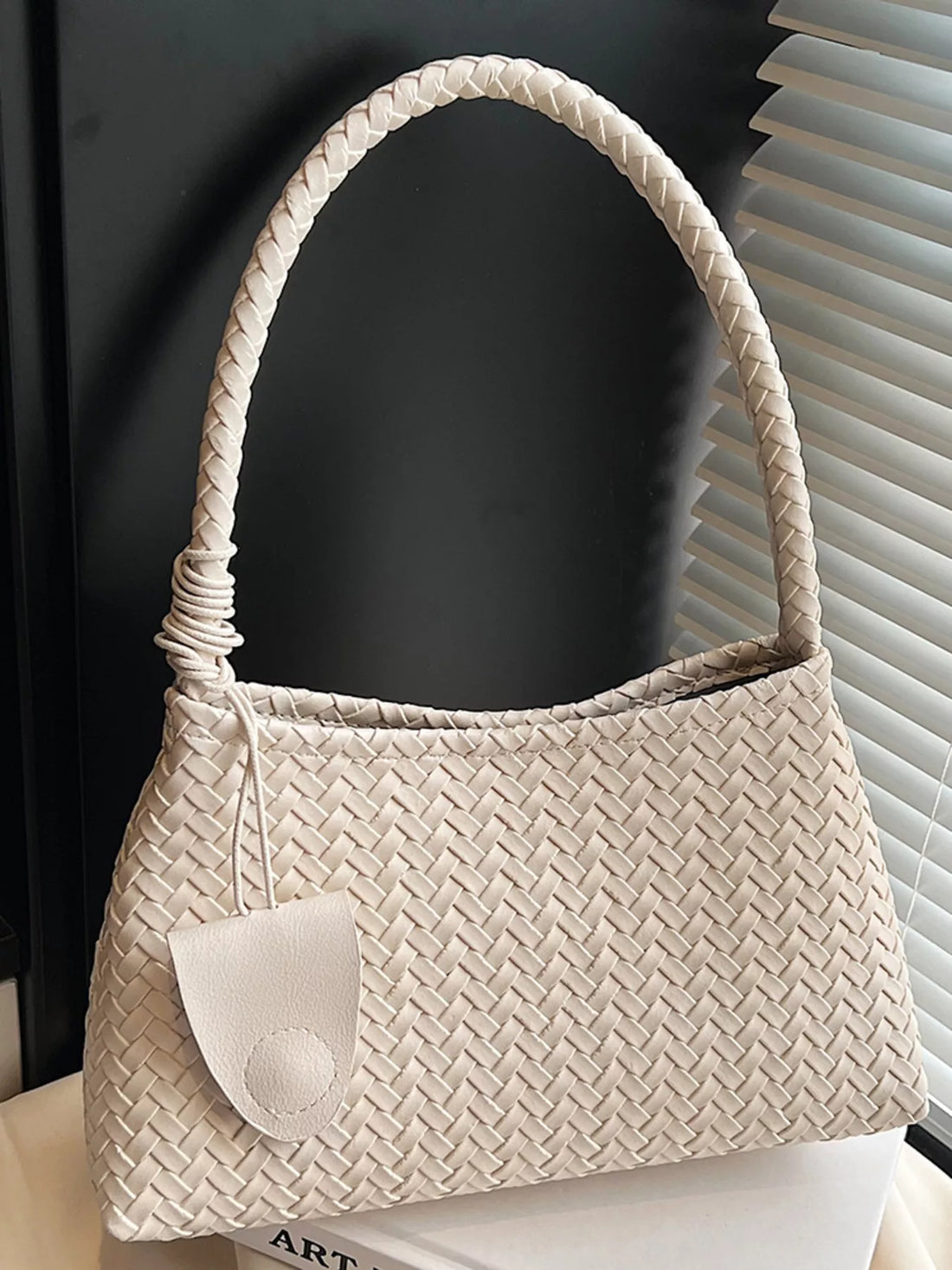 Off-white woven shoulder bag with braided strap and leather fob detail.