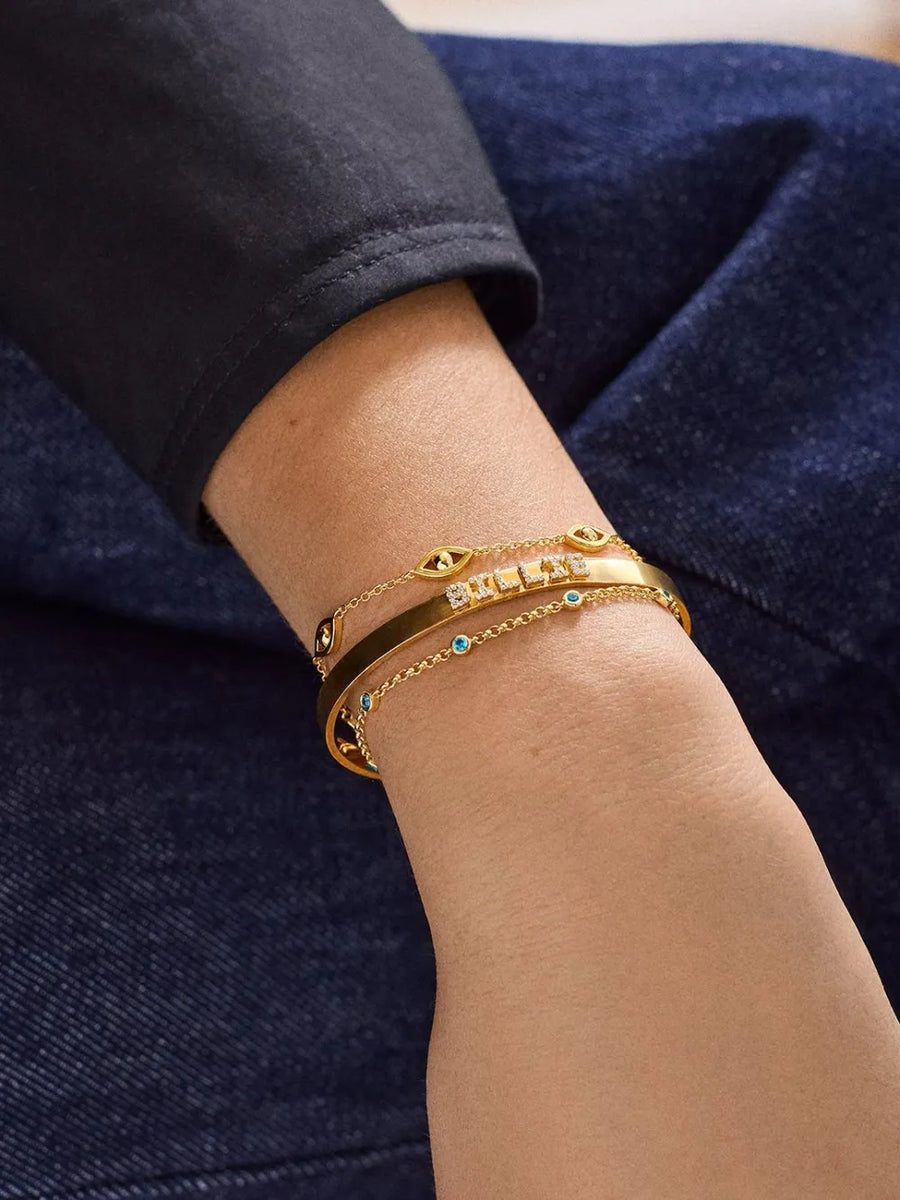 Gold charm chain bracelets with Devil Eye and blue stone details.
