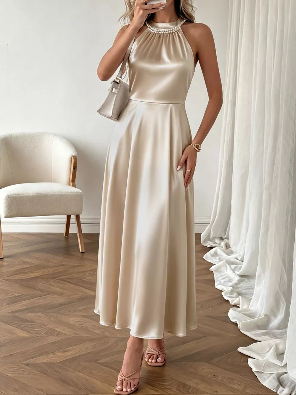 Elegant champagne satin midi dress with pearl halter neckline and A-line skirt.