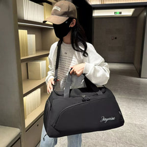 Black waterproof duffel bag with side pockets and embroidered text, held by a person.