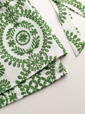 Green tie-waist romper with white leaf print and matching tie detail.