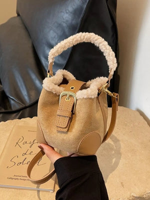 Fuzzy trim crossbody bucket bag in tan suede with leather accents and buckle closure.