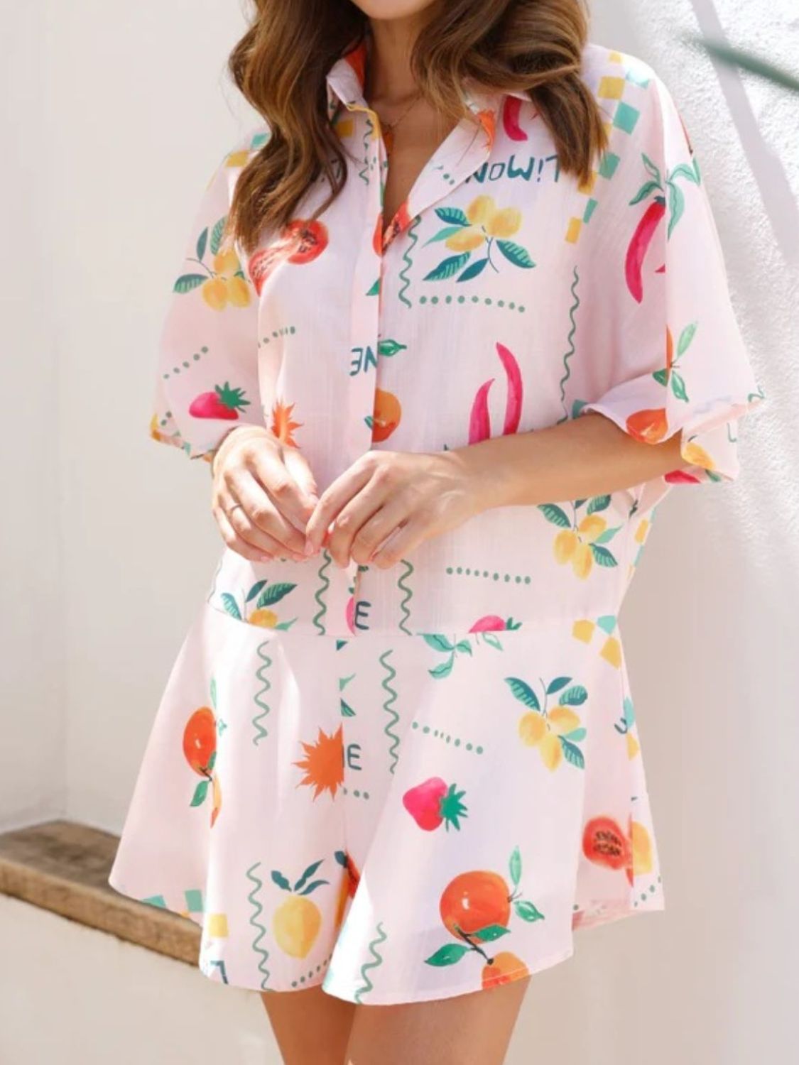 Limoné Print Shirt Romper in blush pink with a fruit and chili pattern, buttoned collared neckline, and short sleeves.