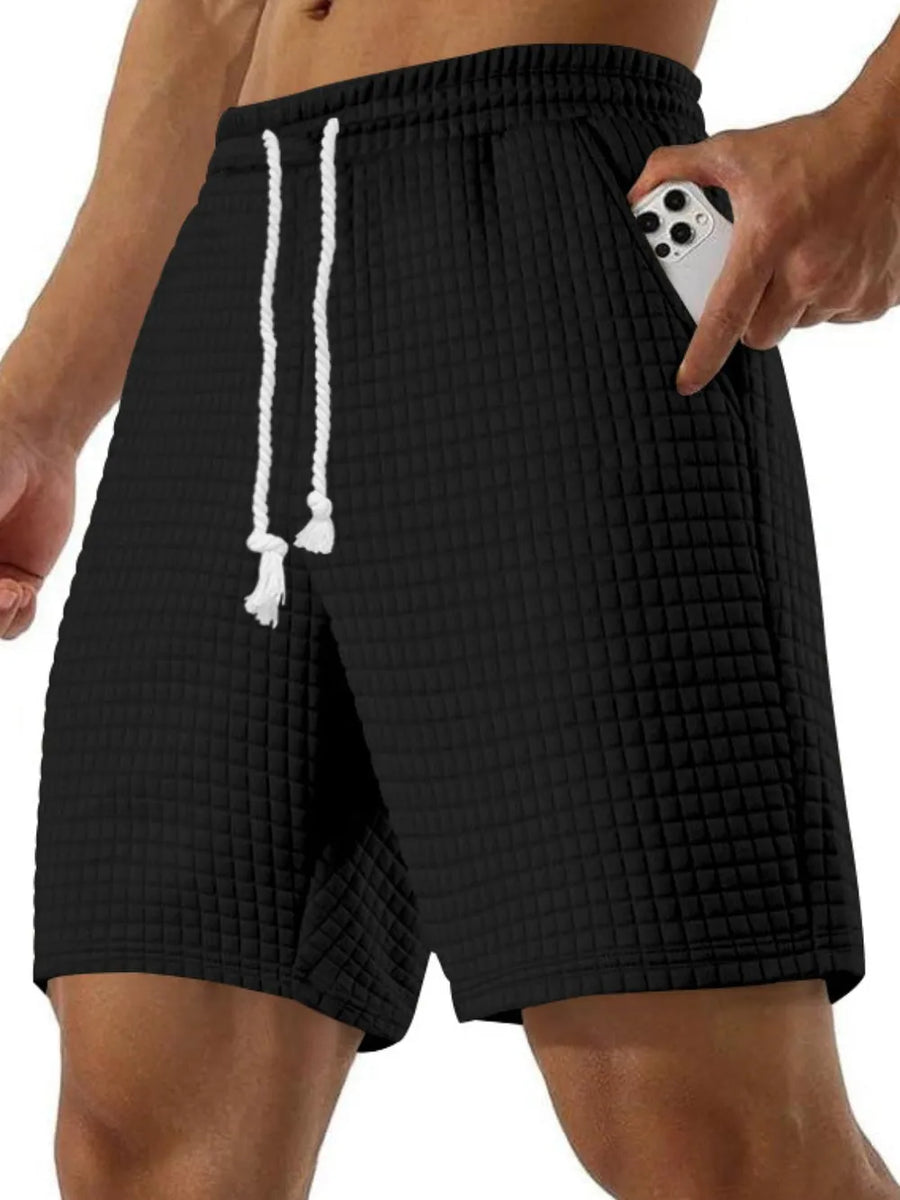 Black waffle knit relaxed fit shorts with drawstring and side pocket detail.