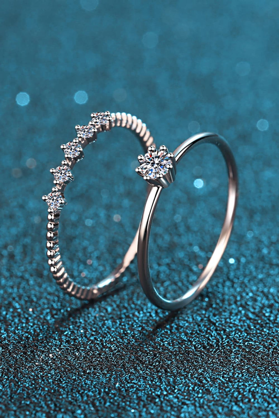 Silver rings set with moissanite stones, one with a starburst design, the other with a celestial row.