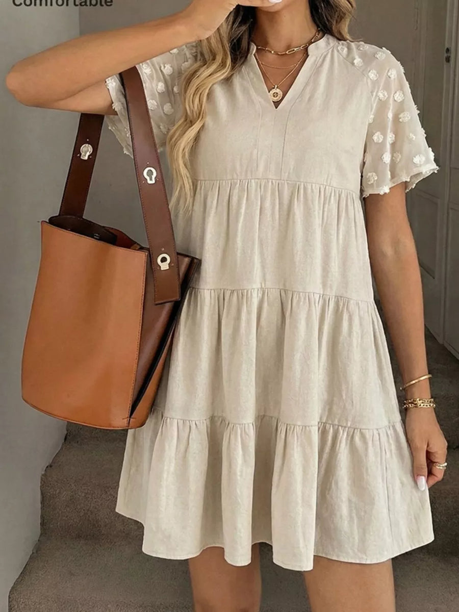 Beige tiered mini dress with sheer dot sleeves and v-neck, cotton blend fabric.