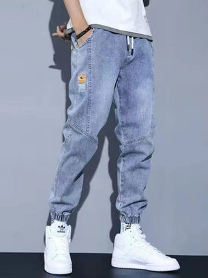 Light wash denim jogger jeans with drawstring and pockets, cuffed ankles.