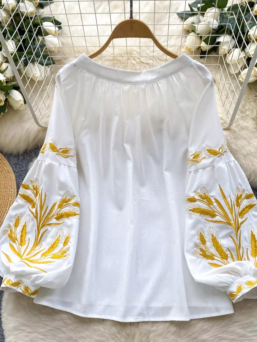 White embroidered tie-neck folk blouse with balloon sleeves and wheat detail.