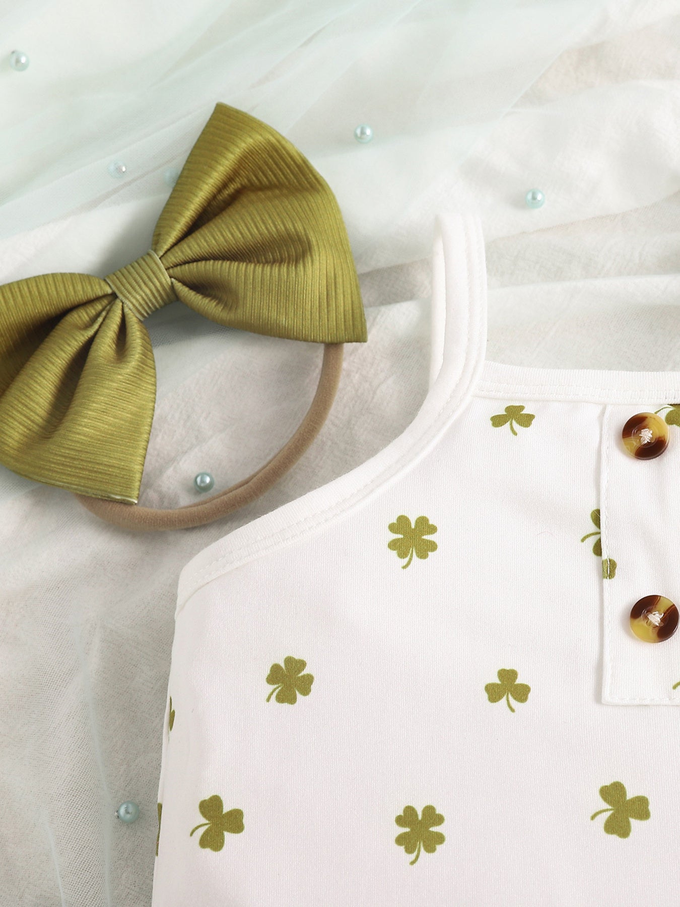White baby bodysuit with green clover print and button detail, paired with a green bow headband.