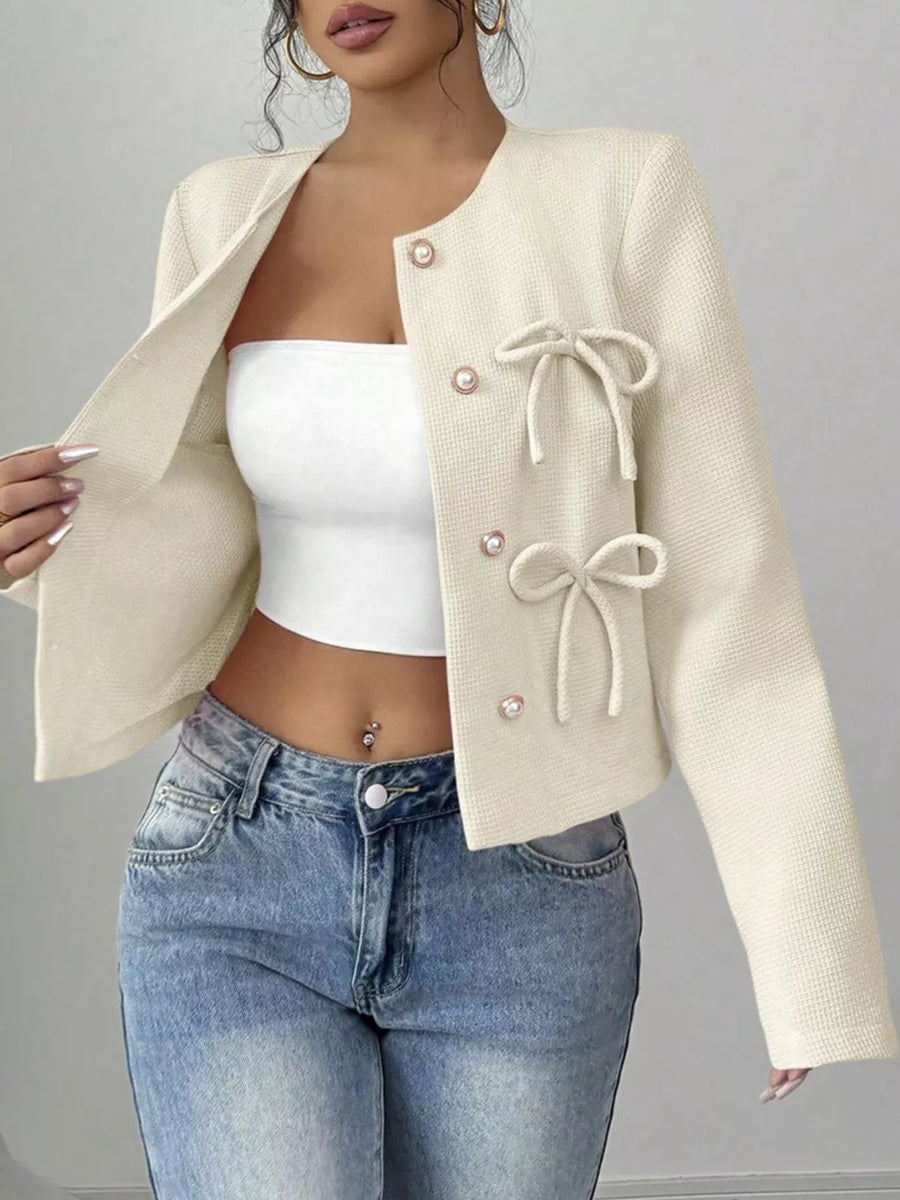 Cream textured cropped jacket with pearl buttons and bow details.
