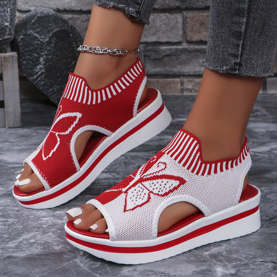 Red and white open-toe wedge sandals with butterfly motif mesh detail and chunky sole.