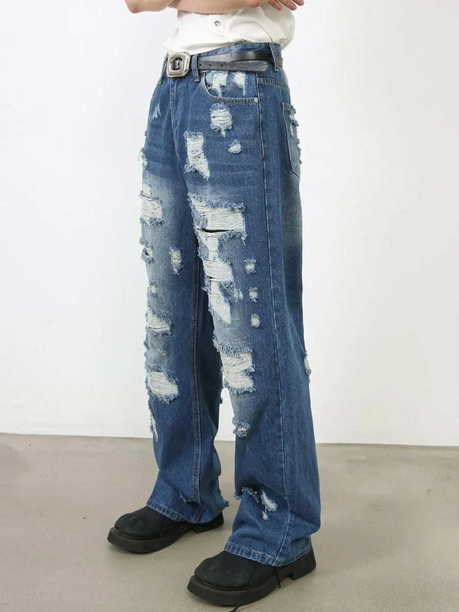 Oversized ripped denim jeans in medium wash with raw edge detail and distressed accents.