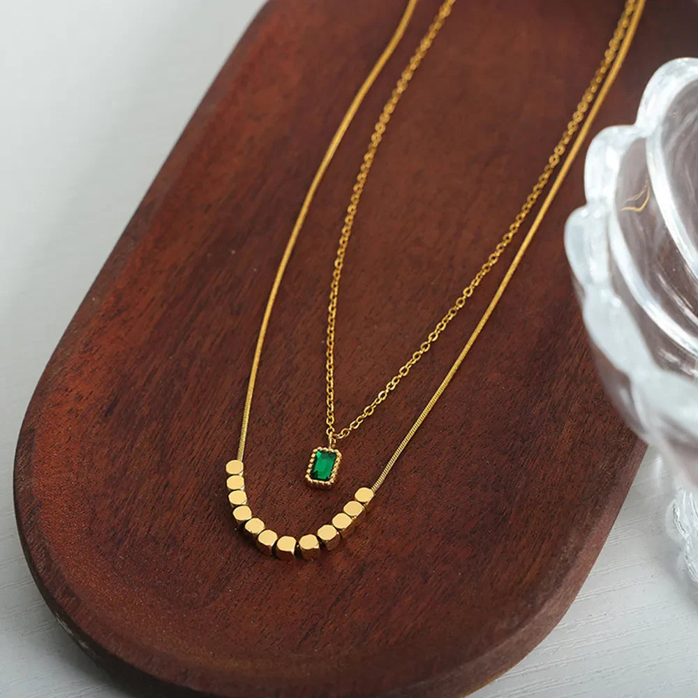 Gold layered necklace with emerald cube pendant and bead accents