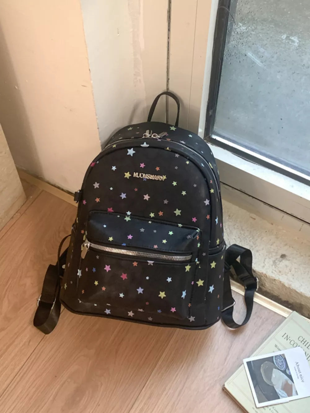 Black mini backpack with colorful star print and front zip pocket.