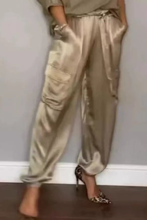 Beige satin cargo pants with drawstring waist and cuffed ankles.