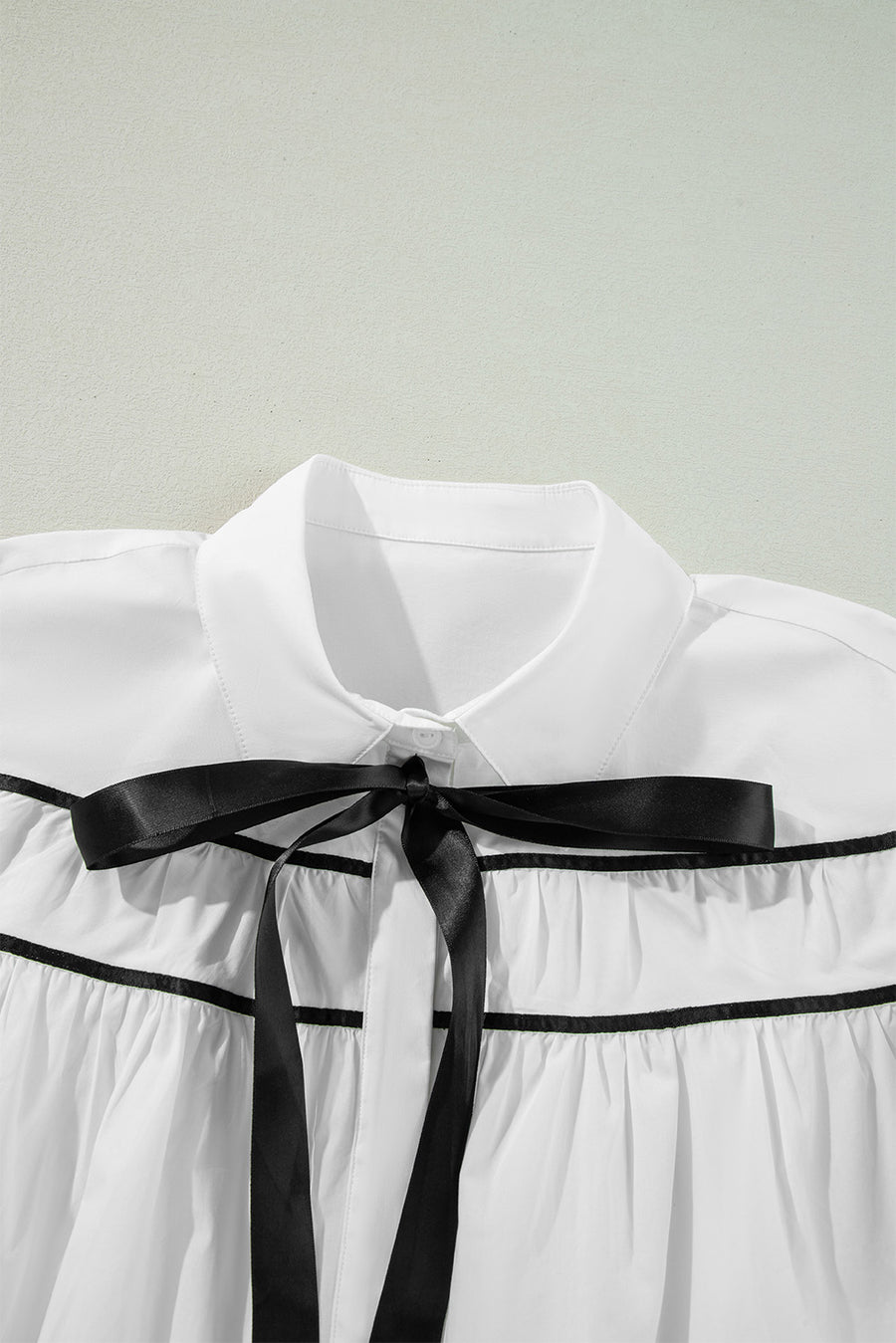 White blouse with black piped trim and a black satin bow detail.
