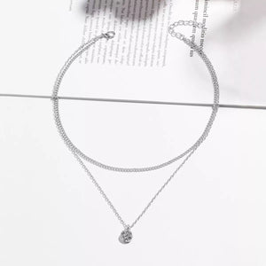 Silver double layered pendant necklace with delicate chains and a small textured pendant.