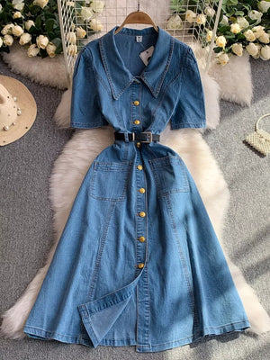 Light blue collared denim midi dress with short sleeves, gold buttons, and a belted waist.