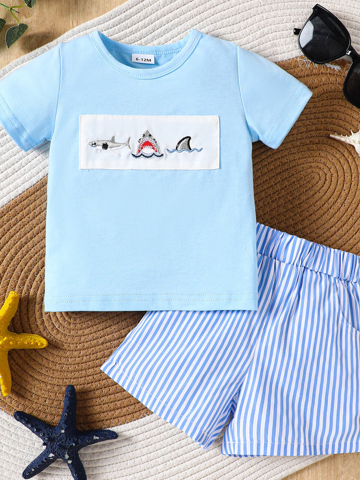 Baby blue cotton t-shirt with embroidered sharks and blue striped shorts.