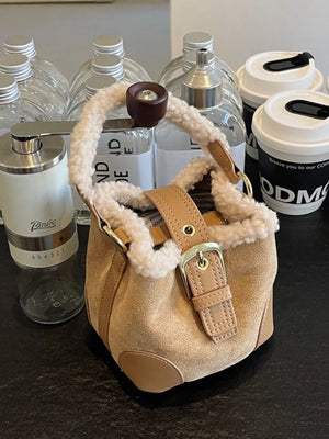 Fuzzy trim crossbody bucket bag in tan suede with leather accents and buckle closure.