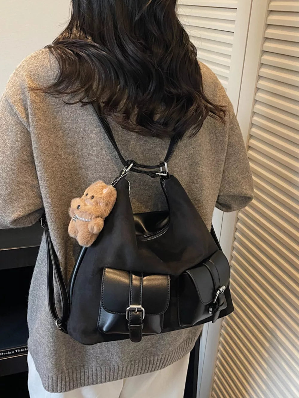 Black suede half-moon bag with multiple buckle pockets and teddy bear charm.