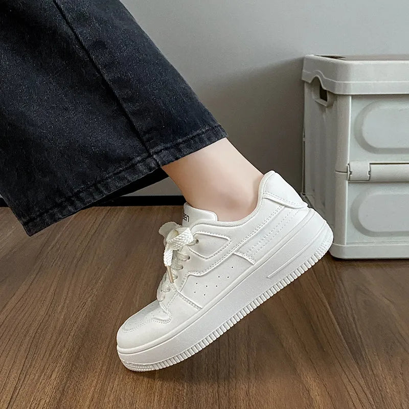 White leather sneakers with perforations and a thick sole, styled with black jeans.