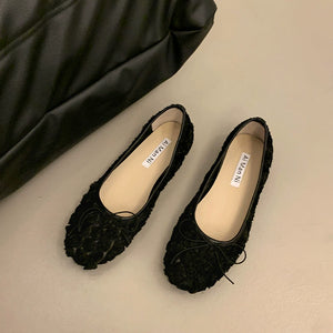 Black slip-on flats with a textured floral pattern and a small bow detail.