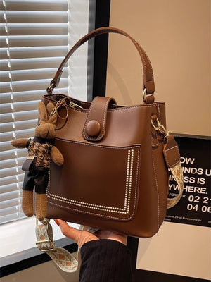 Brown pu leather bucket crossbody bag with decorative studs and a bunny charm.