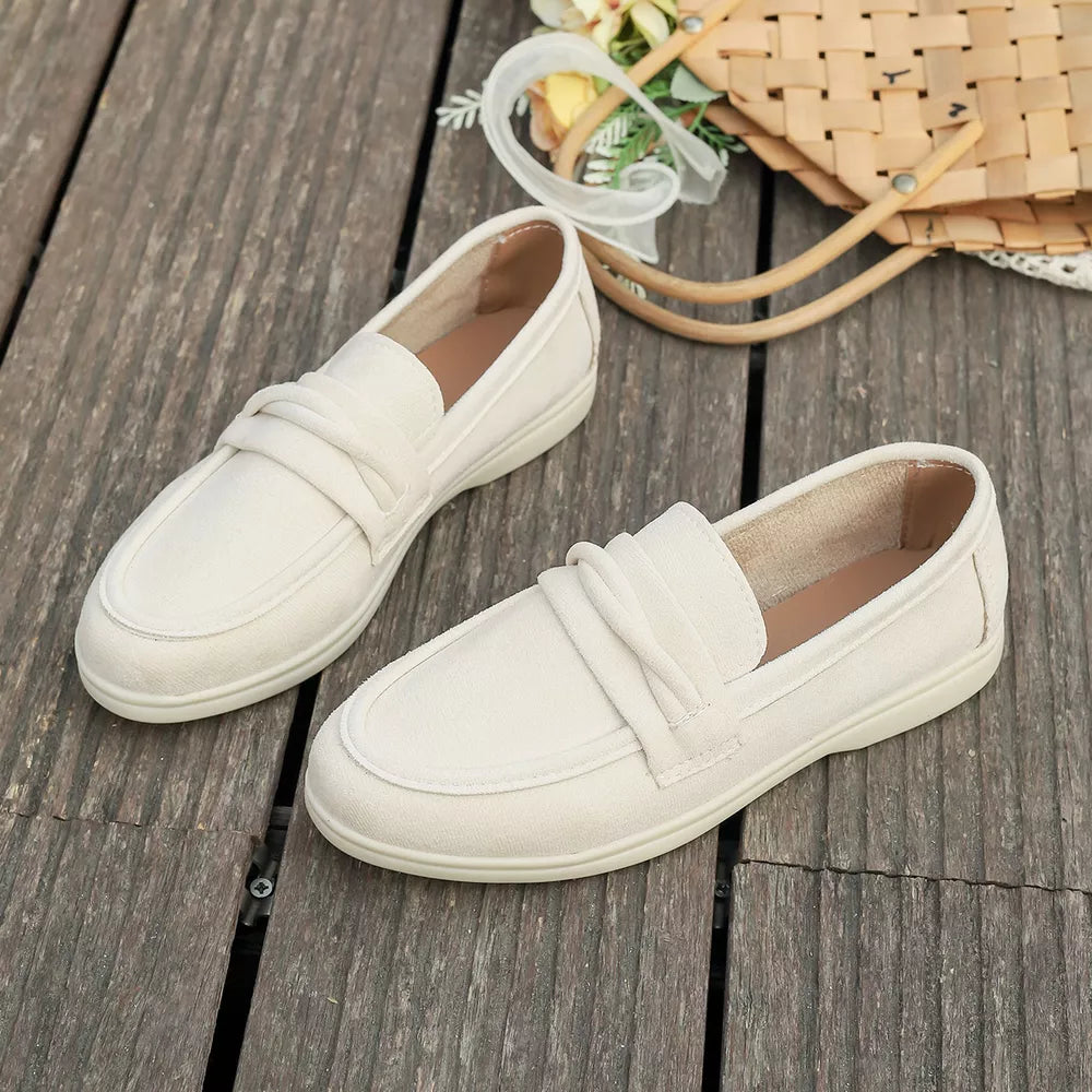 Beige round toe slip-on loafers with decorative strap detail.