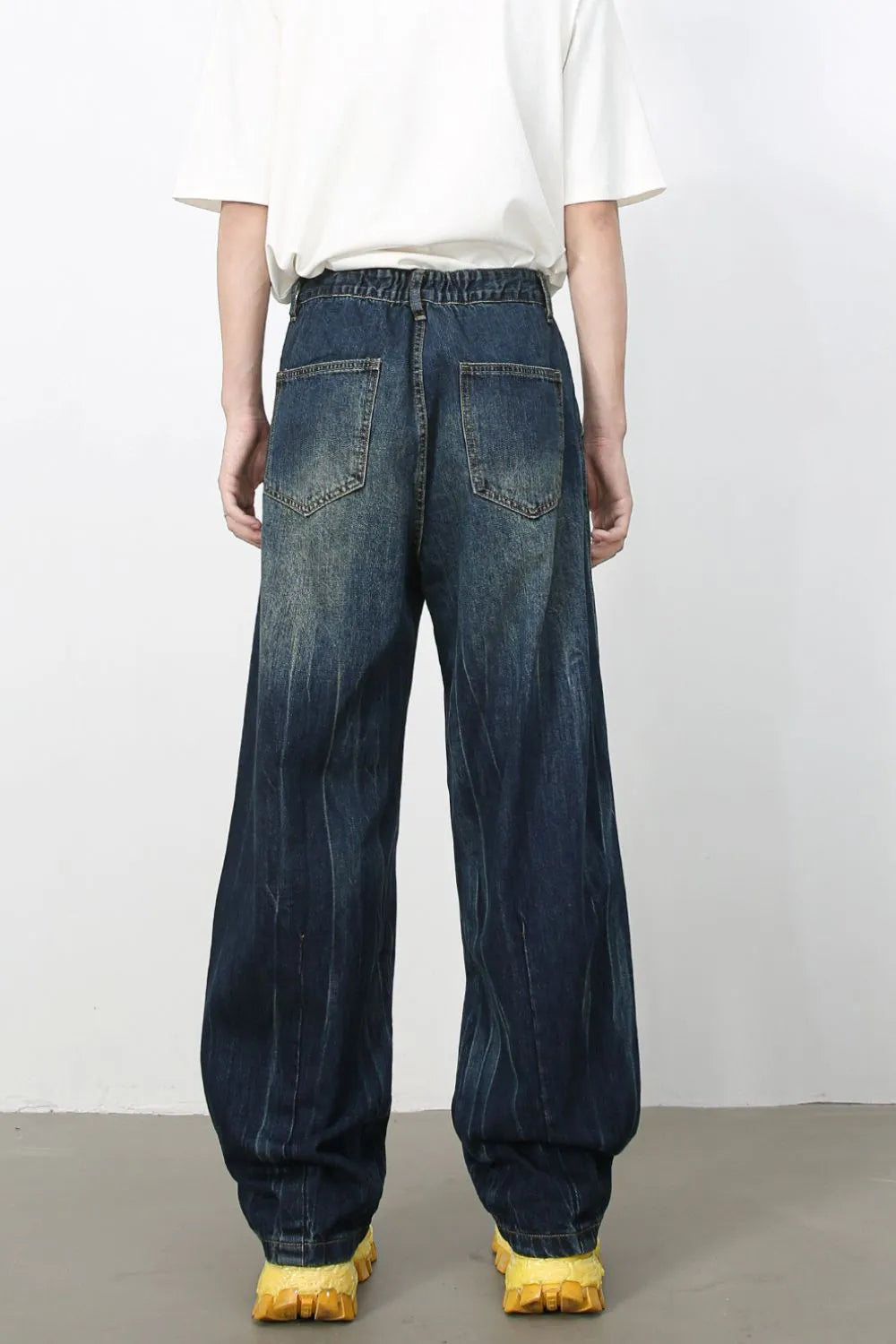 Dark wash pleated wide-leg denim trousers with distressed vertical stripes and elastic waistband.