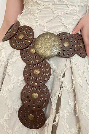 Brown leather belt with embossed medallion and studs, featuring circular cutouts and antique brass hardware.