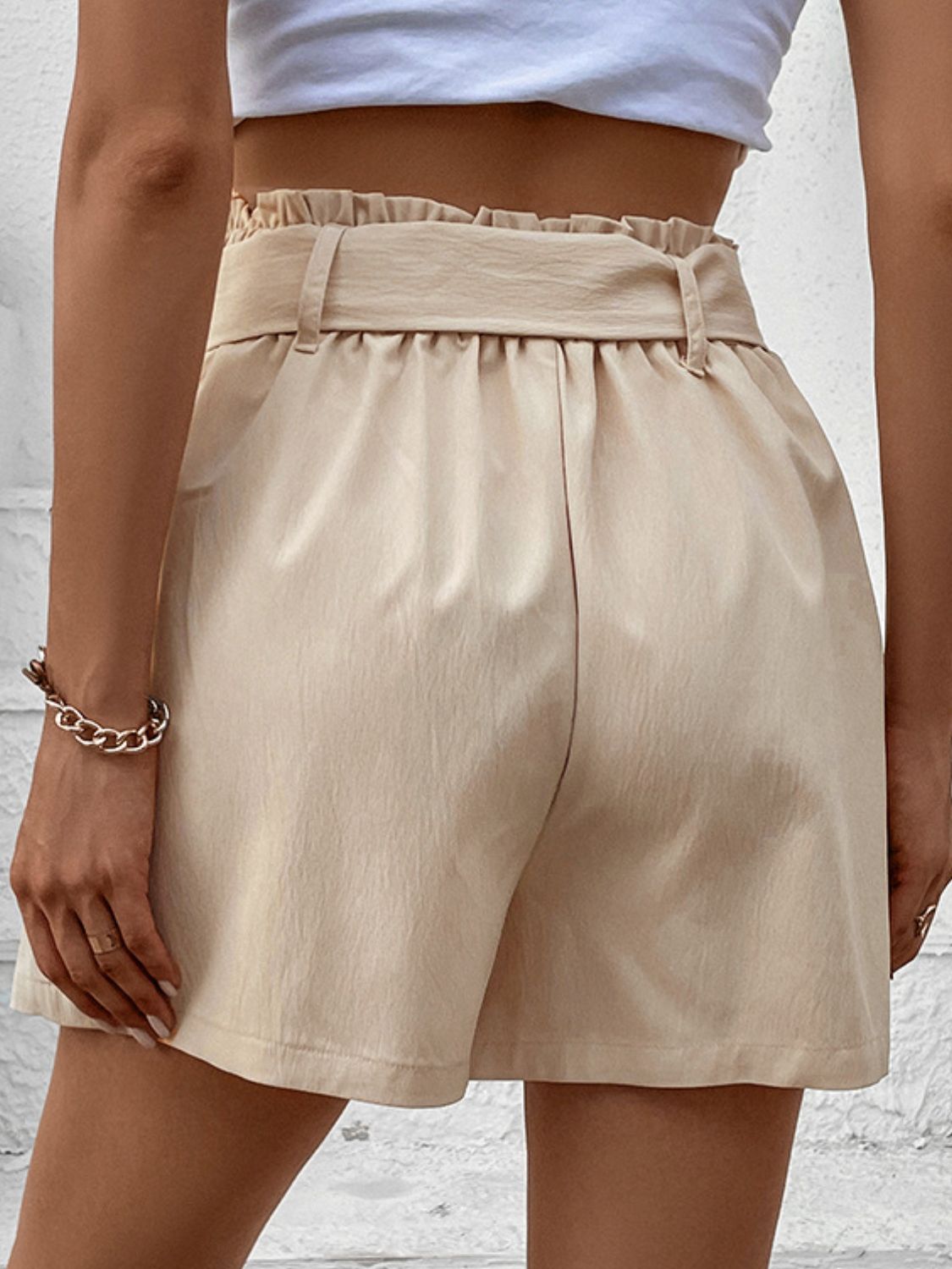 Cream high-waisted pleated belted shorts with ruffled waist detail.