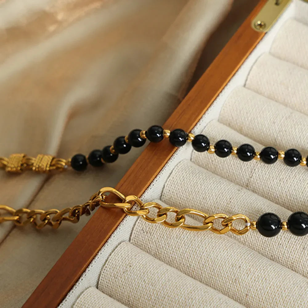 Gold asymmetrical beaded chain necklace with black beads and figaro chain detail.