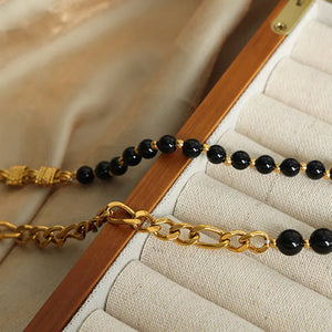 Gold asymmetrical beaded chain necklace with black beads and figaro chain detail.