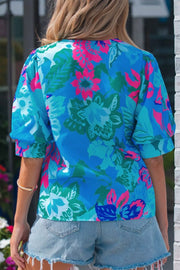 Vibrant floral v-neck blouse with relaxed fit and short puff sleeves, styled with denim shorts.