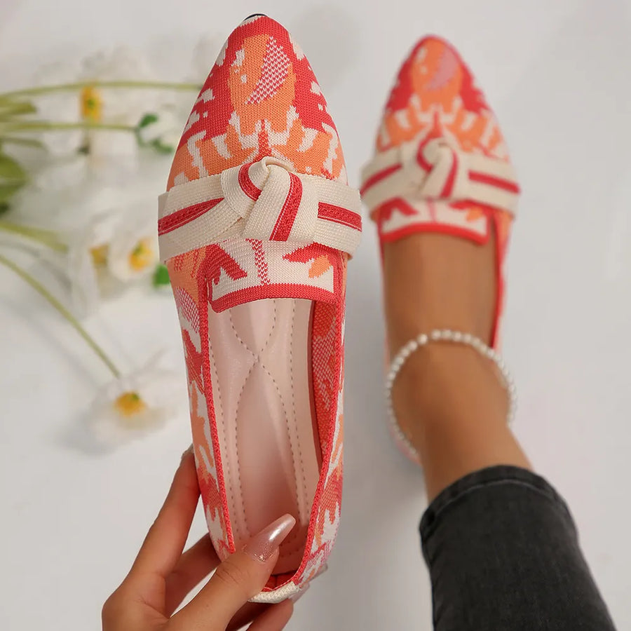 Knitted pointed flats in a coral and white pattern with a cream bow detail.