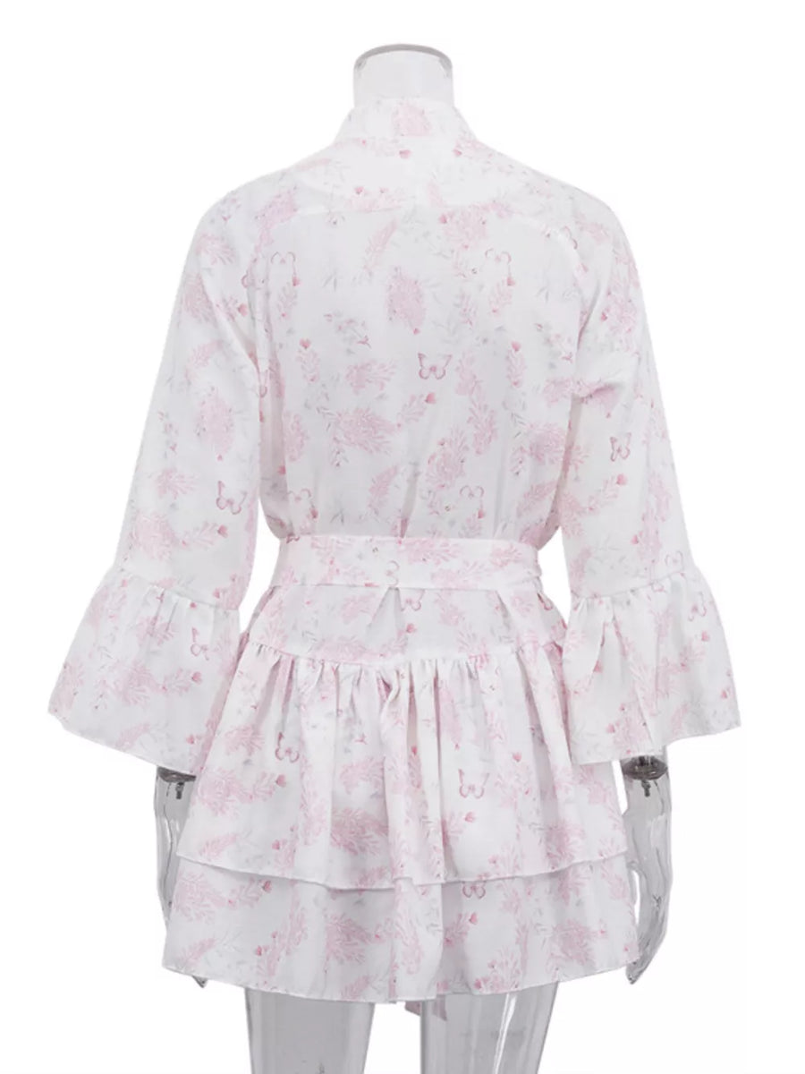 White dress with pink floral and butterfly print, belted waist, tiered ruffled skirt, and bell sleeves.