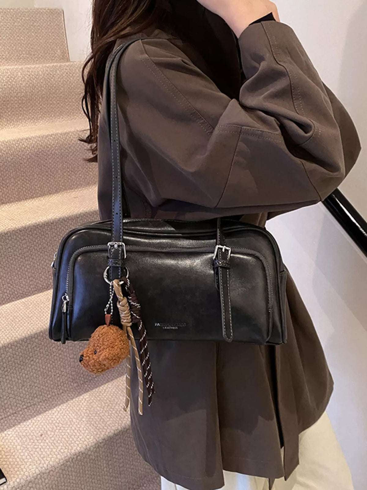 Black leather shoulder bag with buckle details and a teddy bear charm