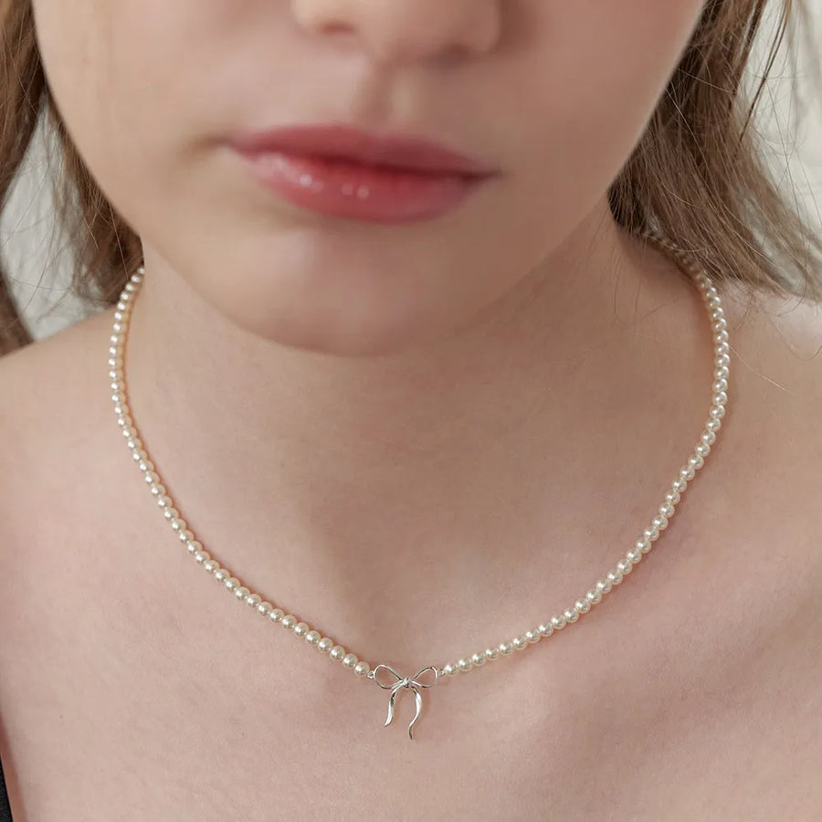 Silver pearl choker necklace with a delicate bow pendant.