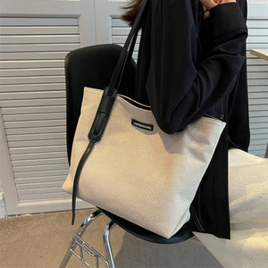 Large canvas shoulder bag with black leather trim and strap detail.