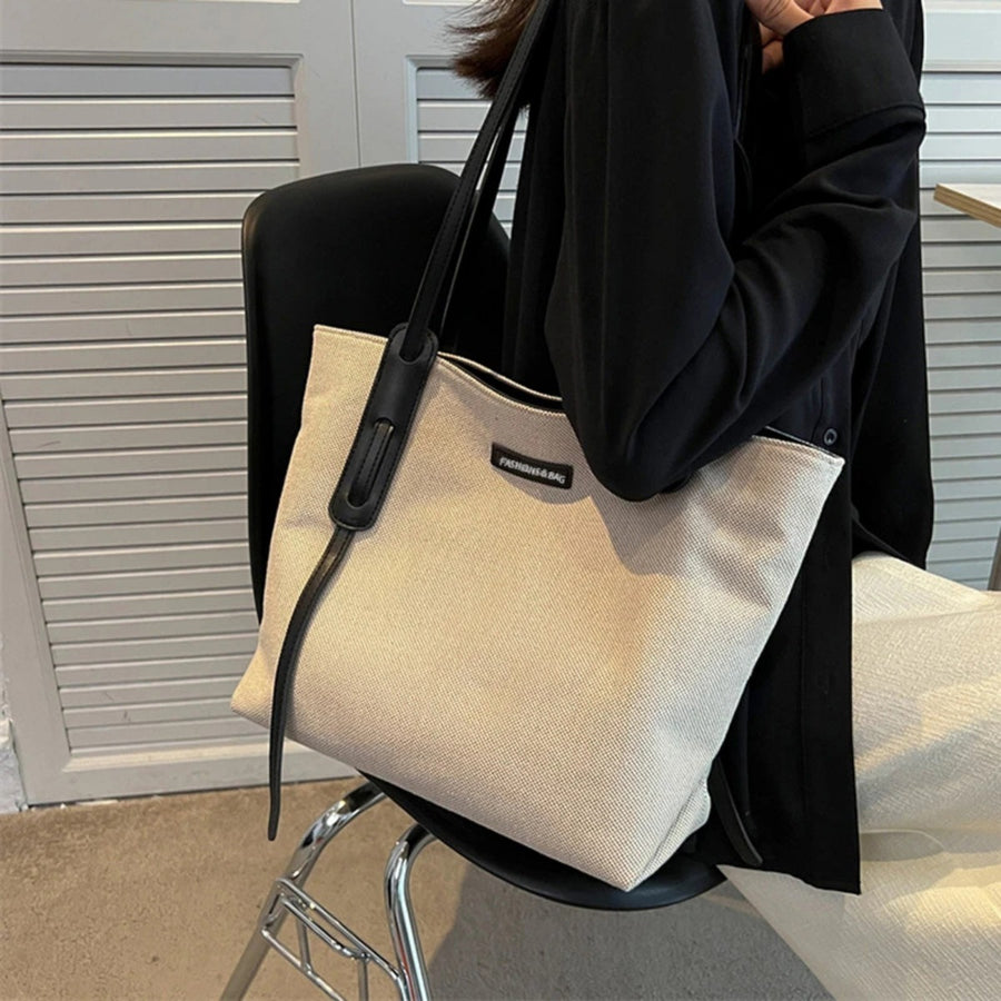 Large canvas shoulder bag with black leather trim and strap detail.