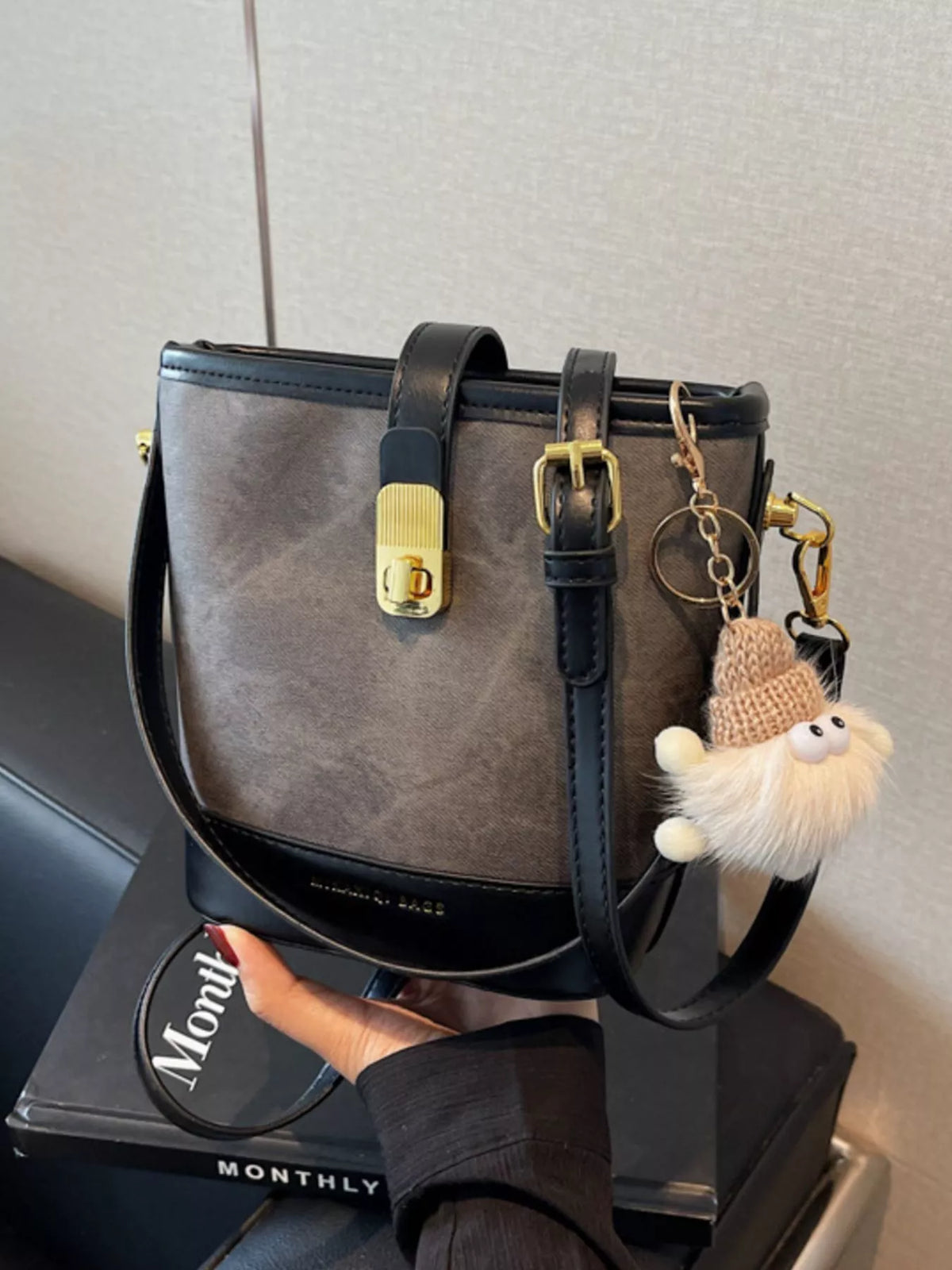Elegant bucket bag in dark brown PU leather with black trim and gold hardware, featuring a playful charm.